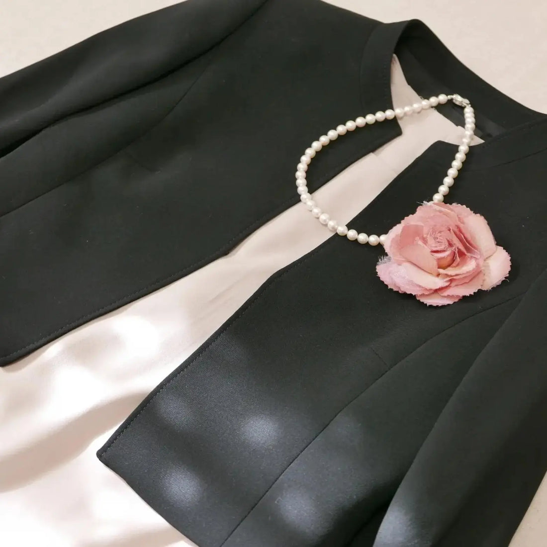 黒のブレザーにピンクの薔薇のブローチと真珠のネックレス。