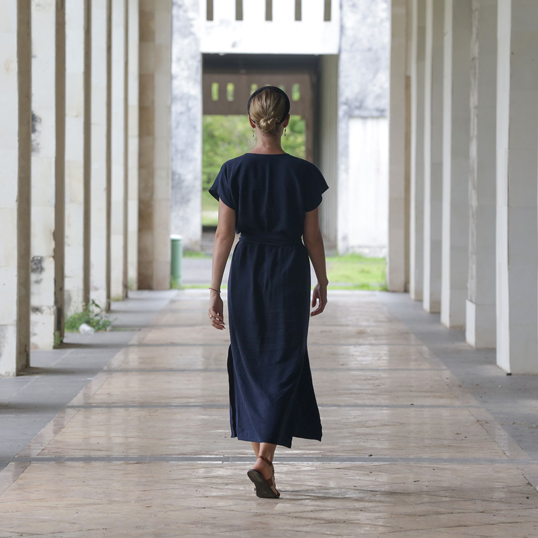 40代の女性が秋の林道を歩む様子を背後から捉えた写真